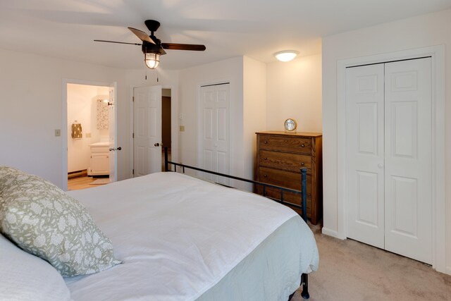 bedroom with two closets, ceiling fan, light carpet, and ensuite bathroom