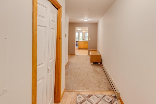 hallway with baseboards, light carpet, and a baseboard radiator