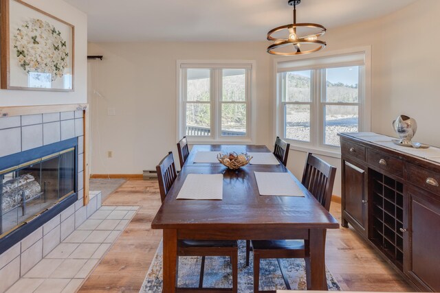 dining area with a healthy amount of sunlight, baseboards, a tiled fireplace, and light wood-type flooring