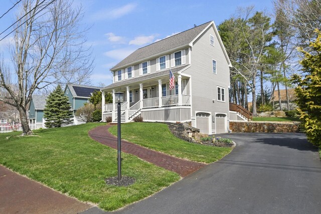 colonial-style house featuring covered porch, driveway, a garage, stairway, and a front lawn