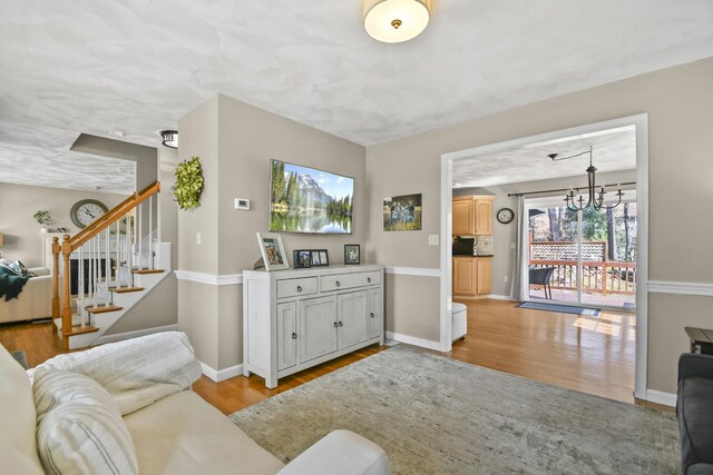 living room with baseboards, light wood finished floors, stairs, and a chandelier