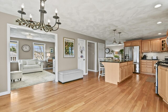 kitchen with dark countertops, appliances with stainless steel finishes, an inviting chandelier, light wood finished floors, and a breakfast bar area
