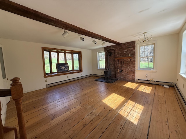 unfurnished living room with baseboard heating, a wood stove, hardwood / wood-style flooring, a baseboard radiator, and a chandelier