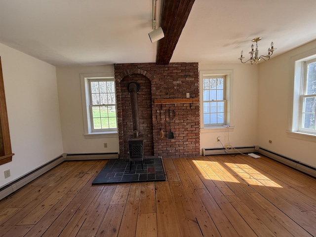 unfurnished living room featuring an inviting chandelier, a wood stove, a wealth of natural light, and hardwood / wood-style floors