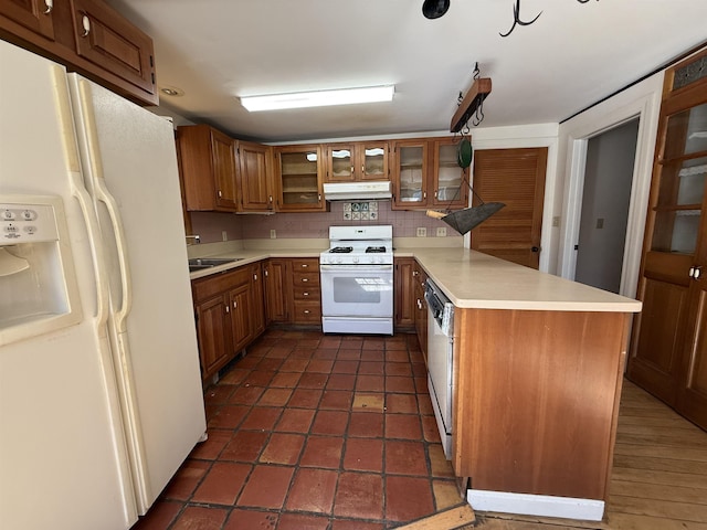kitchen featuring brown cabinets, light countertops, a peninsula, under cabinet range hood, and white appliances