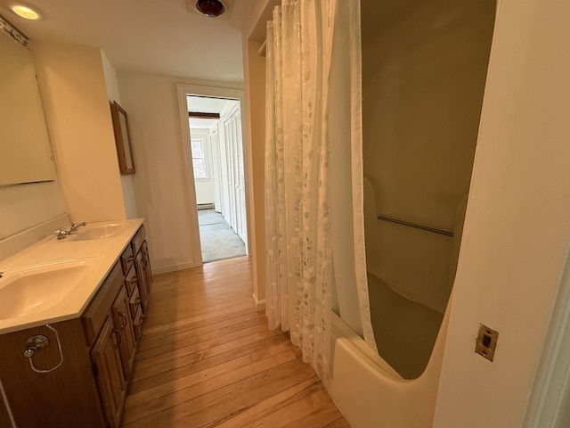 bathroom featuring double vanity, a sink, hardwood / wood-style flooring, and shower / tub combo