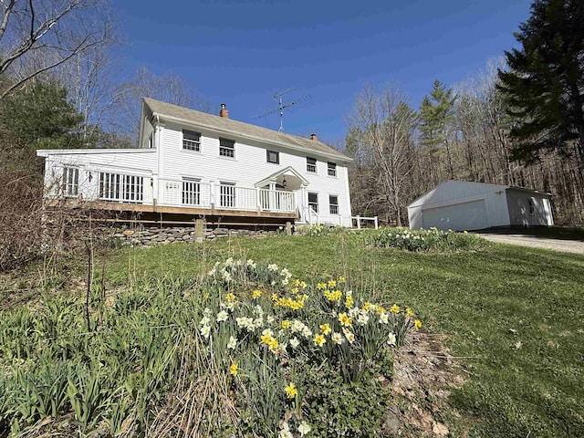 back of property featuring a detached garage, a deck, an outbuilding, and a chimney