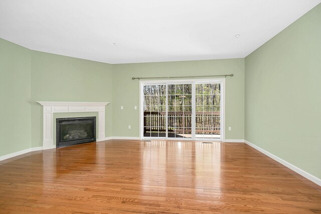 unfurnished living room with baseboards, a glass covered fireplace, and wood finished floors