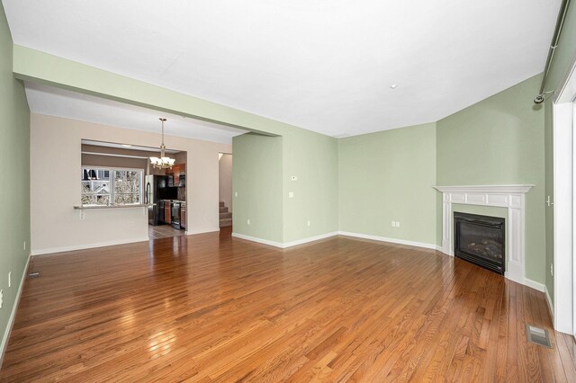 unfurnished living room with a glass covered fireplace, visible vents, wood finished floors, and a chandelier