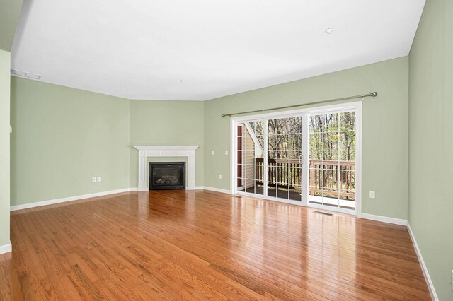 unfurnished living room featuring baseboards, a glass covered fireplace, wood finished floors, and visible vents