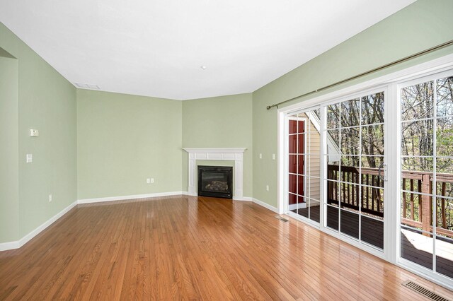 unfurnished living room with a glass covered fireplace, baseboards, wood finished floors, and visible vents