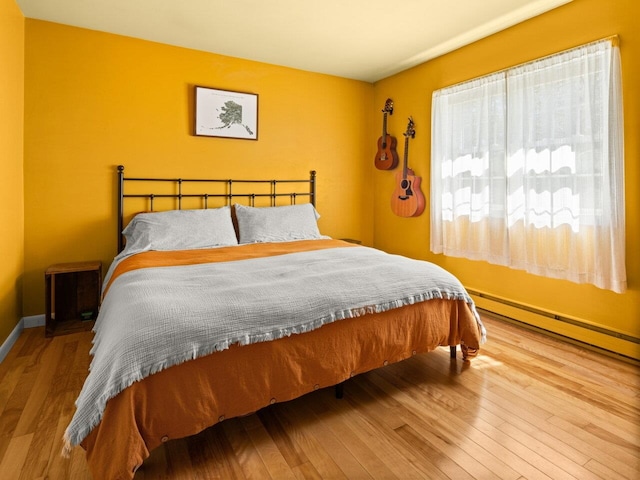 bedroom with baseboard heating, baseboards, and wood finished floors