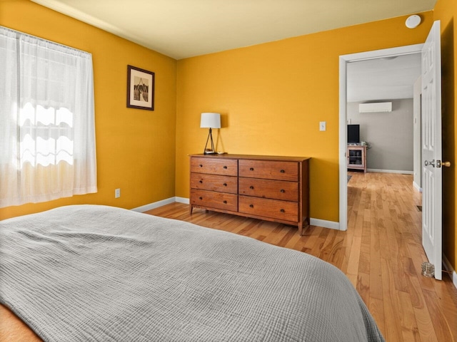 bedroom with baseboards, a wall mounted air conditioner, and wood finished floors