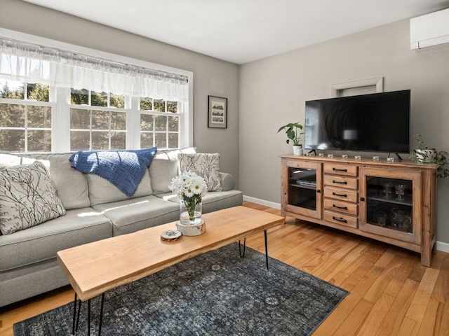living area featuring light wood-style floors, baseboards, and a wall mounted air conditioner