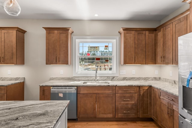 kitchen with brown cabinetry, light stone counters, a sink, light wood-style flooring, and stainless steel appliances