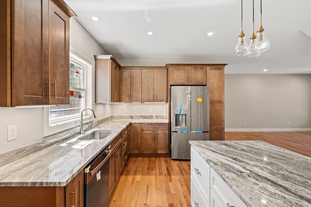 kitchen featuring brown cabinetry, light stone countertops, a sink, light wood finished floors, and appliances with stainless steel finishes