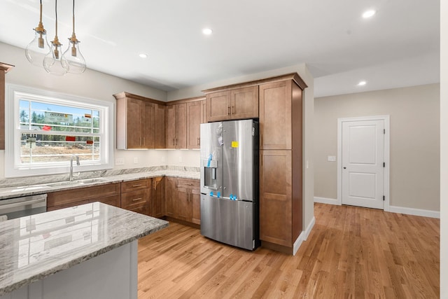kitchen featuring light wood-style floors, a sink, light stone counters, and stainless steel appliances