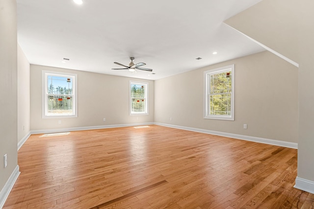 empty room with baseboards, a ceiling fan, light wood-style flooring, and a wealth of natural light