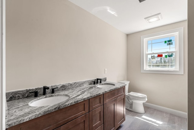 bathroom with a sink, baseboards, toilet, and double vanity