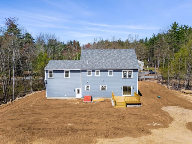 rear view of house with a deck, a wooded view, and a shingled roof