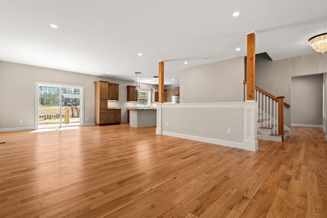 unfurnished living room with recessed lighting, light wood-style floors, stairway, and an inviting chandelier