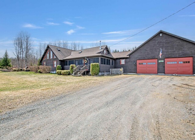view of front of home with a garage, dirt driveway, and roof with shingles