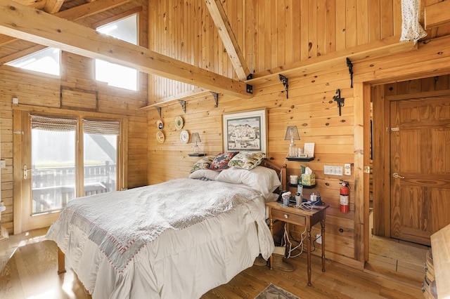 bedroom featuring wooden walls, beamed ceiling, multiple windows, and wood finished floors