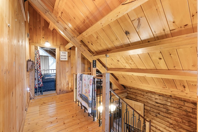hallway with wood walls, light wood-style flooring, an upstairs landing, vaulted ceiling with beams, and wood ceiling