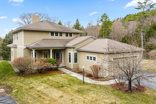 view of front of home featuring a porch, an attached garage, a chimney, and a front lawn