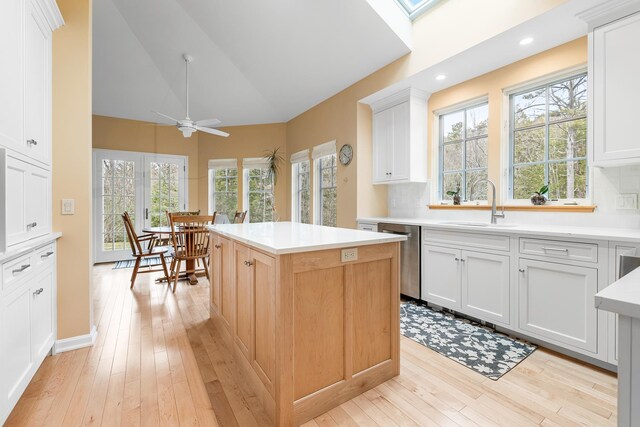 kitchen with ceiling fan, a kitchen island, stainless steel dishwasher, a sink, and light wood-style floors