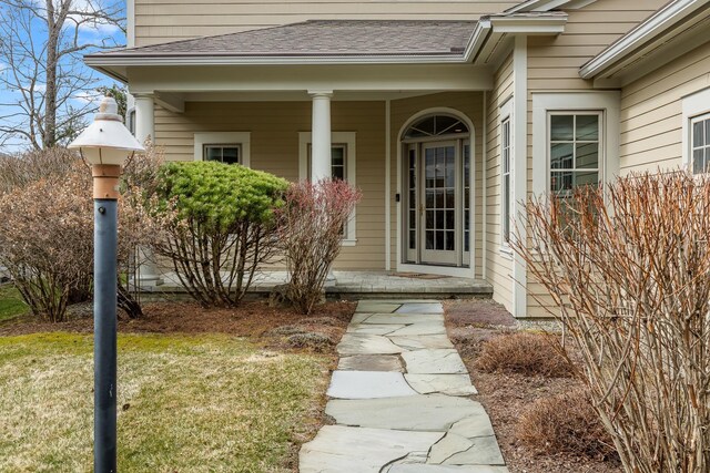 view of exterior entry with a lawn, a shingled roof, and covered porch
