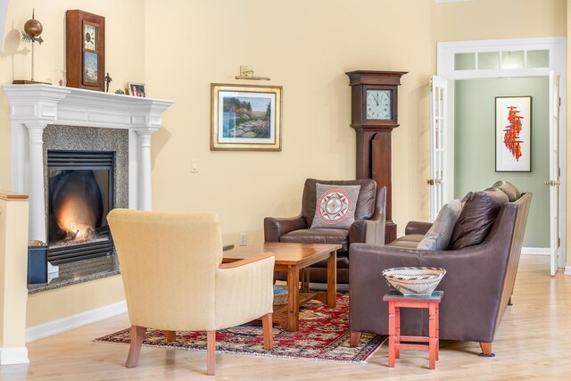 living area with baseboards, a glass covered fireplace, and light wood-type flooring