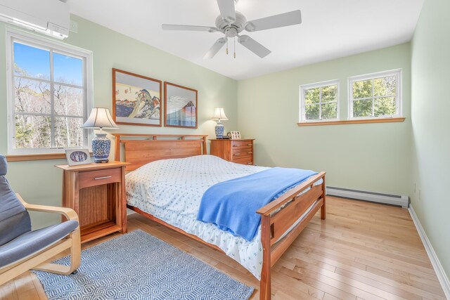 bedroom with a ceiling fan, light wood-style floors, a wall mounted AC, and a baseboard radiator