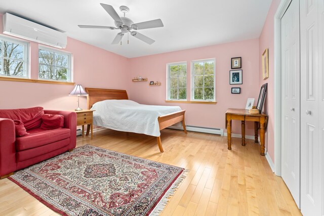 bedroom with a ceiling fan, a baseboard radiator, a closet, an AC wall unit, and light wood-style flooring