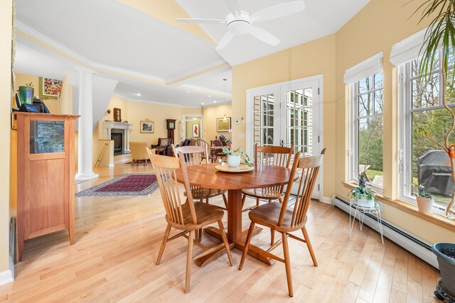 dining room with a fireplace, baseboard heating, light wood-type flooring, and a wealth of natural light