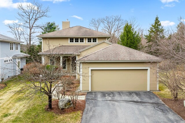traditional-style house with a shingled roof, a garage, a porch, a chimney, and driveway