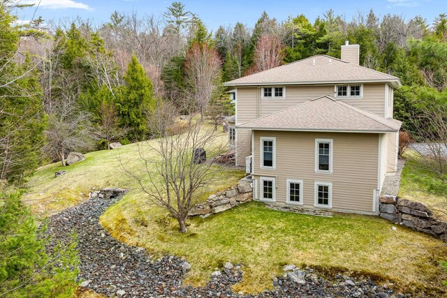 rear view of property with a shingled roof, a yard, and a chimney