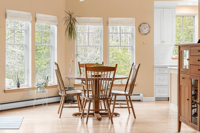 dining room with a baseboard heating unit, a healthy amount of sunlight, and light wood finished floors