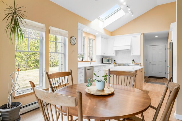 dining space with light wood finished floors, rail lighting, a toaster, a baseboard heating unit, and lofted ceiling with skylight
