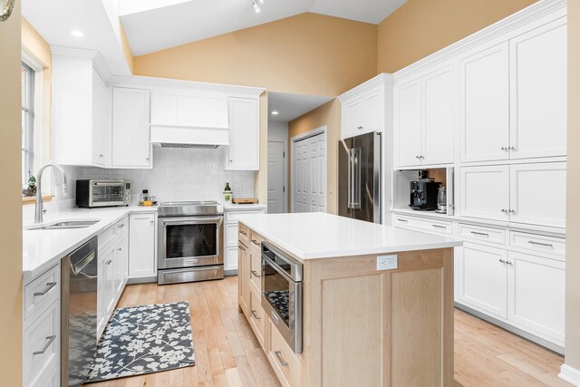 kitchen featuring backsplash, vaulted ceiling, a sink, light wood-style floors, and stainless steel appliances