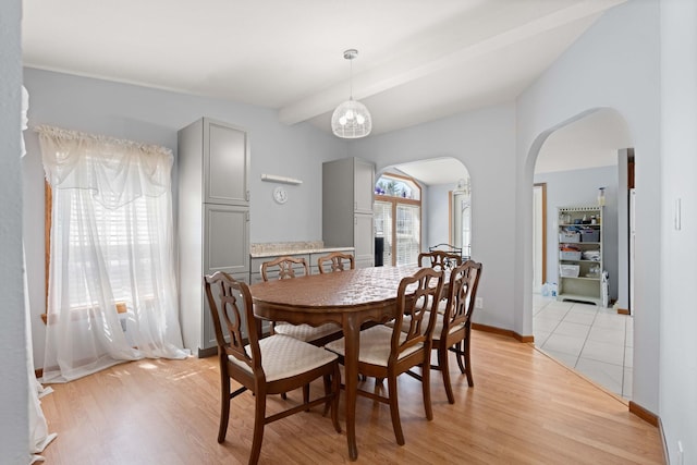 dining space featuring arched walkways, baseboards, beam ceiling, and light wood finished floors