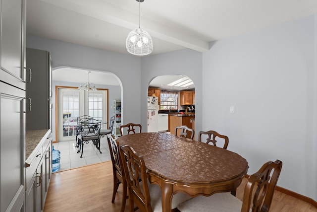 dining room with light wood-style floors, arched walkways, and a chandelier