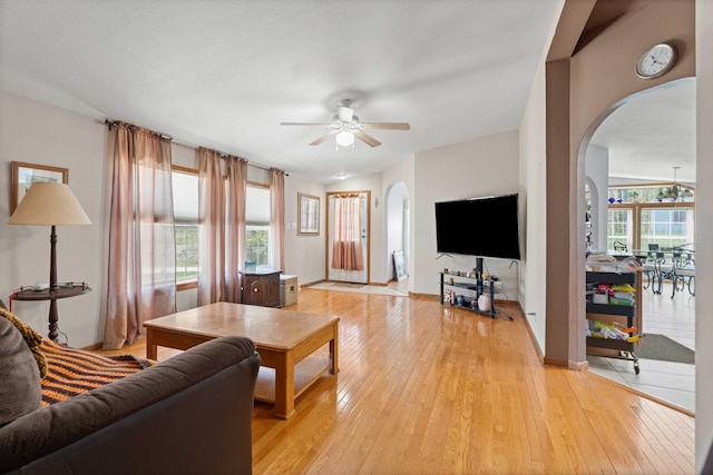 living room featuring arched walkways, ceiling fan, and light wood-style flooring