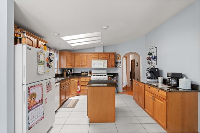 kitchen with a kitchen island, white appliances, dark stone counters, arched walkways, and vaulted ceiling