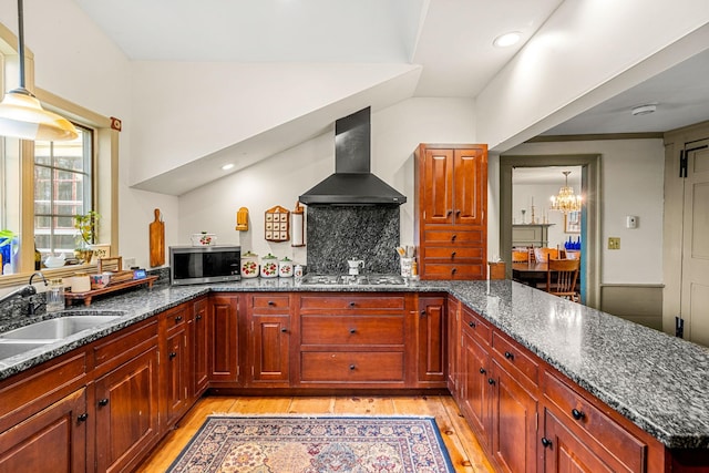 kitchen with wall chimney range hood, an inviting chandelier, a sink, stainless steel appliances, and light wood-type flooring