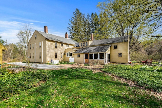 rear view of house featuring a yard, a patio, a chimney, and a sunroom