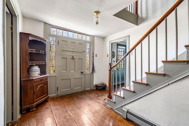 foyer entrance featuring wood-type flooring, a baseboard heating unit, and stairway
