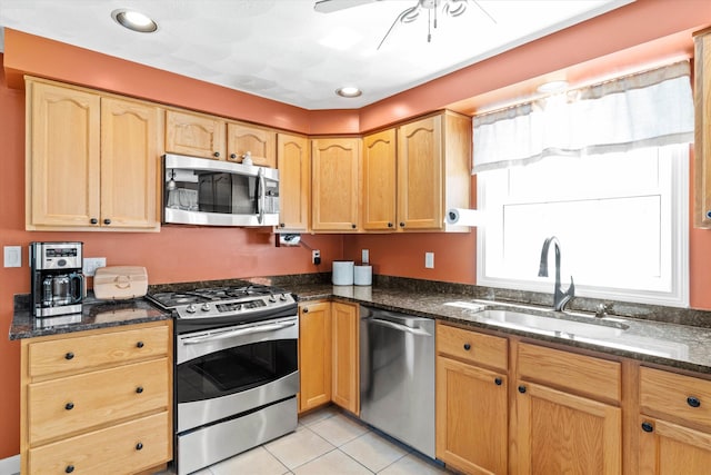 kitchen featuring light tile patterned flooring, ceiling fan, a sink, dark stone countertops, and stainless steel appliances