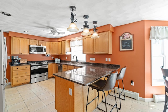 kitchen featuring appliances with stainless steel finishes, baseboard heating, a sink, a peninsula, and light tile patterned floors