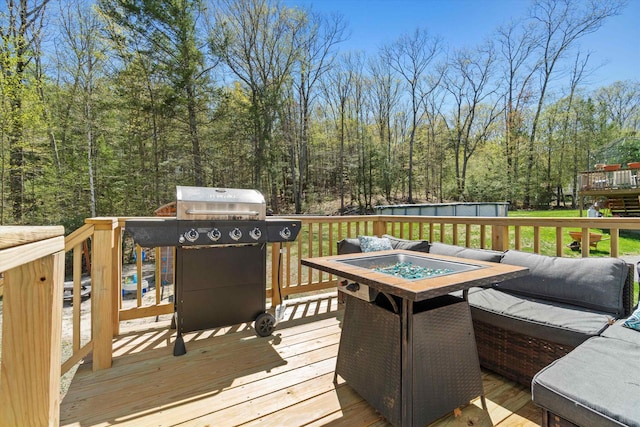 wooden terrace with a view of trees, a fire pit, and area for grilling